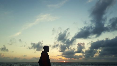 Silhouette man standing by sea against sky during sunset