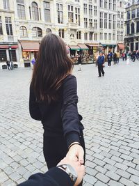 Cropped image of man holding woman hand on street against buildings