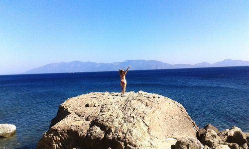 Woman jumping on beach against clear blue sky