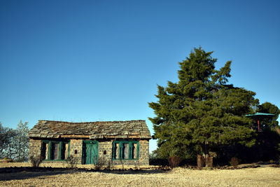 House and trees on field against clear blue sky