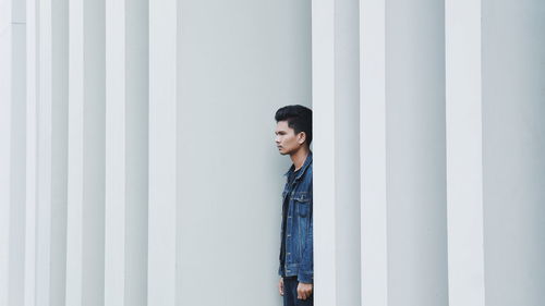 Side view of young man standing at architectural columns