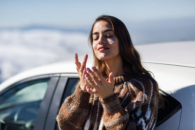 Young woman applying moisturizer on face during winter