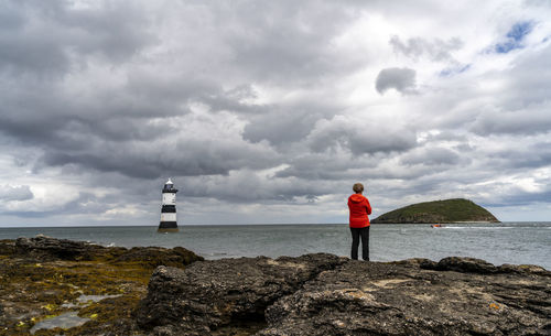 Woman standing on rock by sea against sky