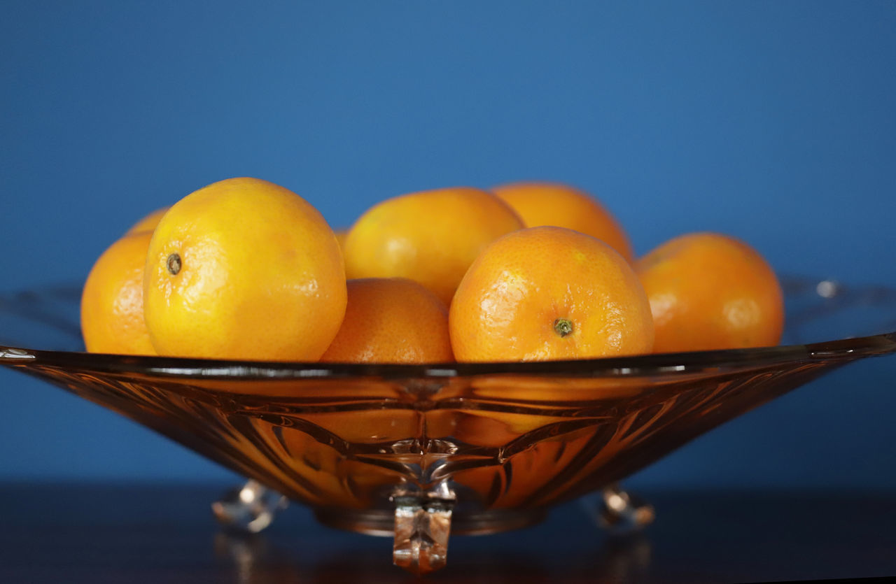 CLOSE-UP OF ORANGE FRUIT IN BOWL AGAINST BLUE BACKGROUND