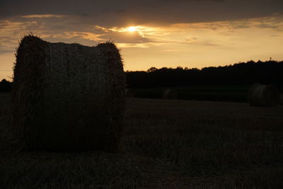 Hay bales on field against sky during sunset