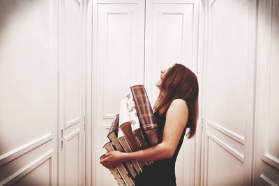 Side view of woman with books laughing while standing by door