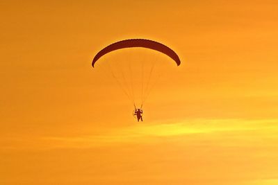 Low angle view of person paragliding against orange sky