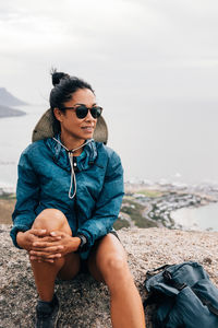 Smiling woman sitting on rock by cliff against town