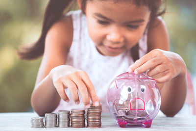 Girl putting coin in piggy bank at table