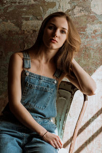 Portrait of young woman sitting on chair against wall