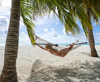 Mid adult woman relaxing on hammock at beach against sky