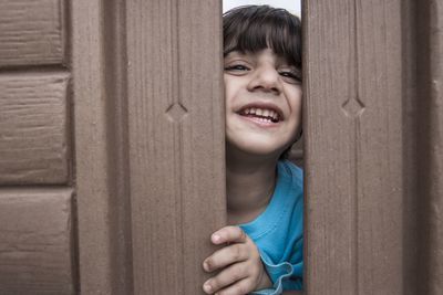 Portrait of smiling boy peeking through wooden fence