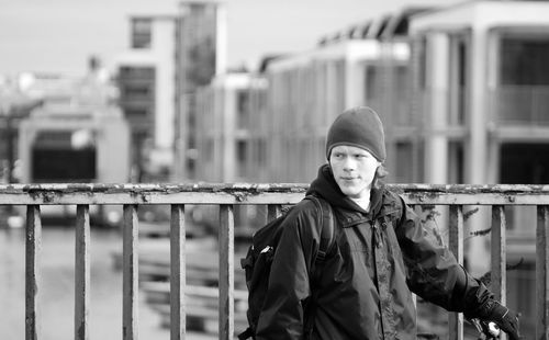 Portrait of young man standing against railing in city
