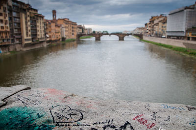 Graffiti on retaining wall by arno river against cloudy sky