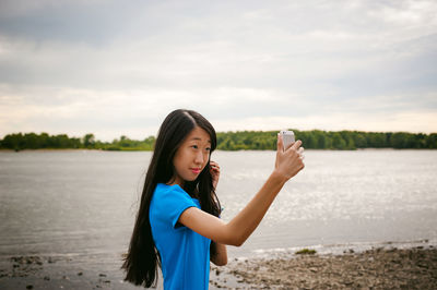 Young woman taking selfie while standing at riverbank