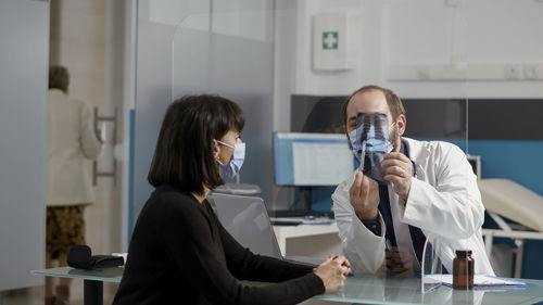 Doctor discussing over x-ray with female patient in hospital during covid-19