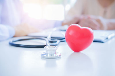 Close-up of red heart model at desk while doctor and patient in background