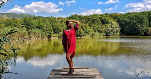 Woman posing while standing on pier at lake against sky