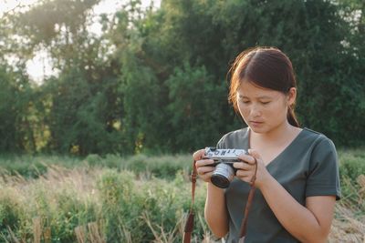 Young woman with camera standing against trees in forest