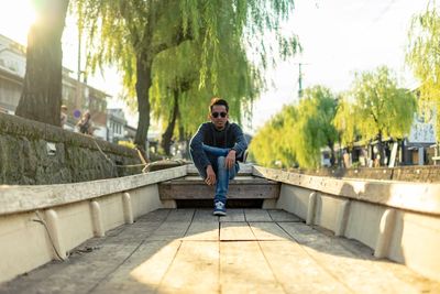 Portrait of young man on retaining wall against trees