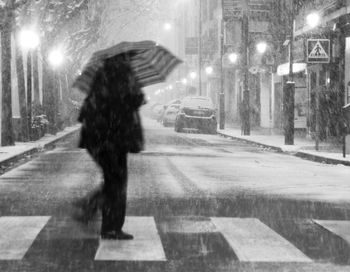 Rear view of woman walking on city street during rainy season