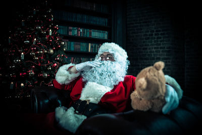 Man wearing santa claus costume smoking on sofa at home