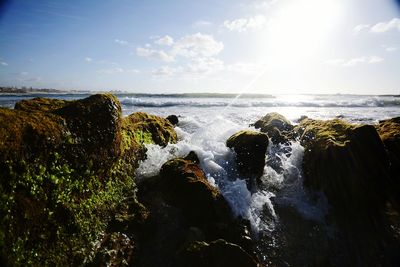 Scenic view of waves splashing on rocks in sea against sky