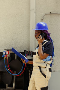 Side view of young woman using mobile phone while standing against wall