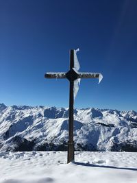 Cross on snowcapped mountain against clear blue sky