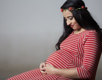 Young pregnant woman smiling while sitting against gray wall