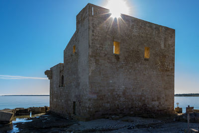 Old building by sea against clear blue sky