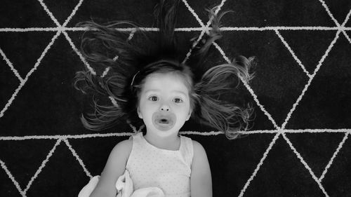 High angle view of girl with pacifier lying on bed