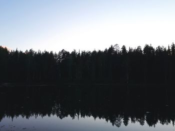 Reflection of silhouette trees in lake against clear sky