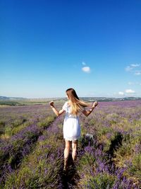 Rear view of young woman standing on lavender field against sky
