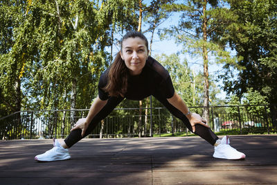 Girl in sportswear on a sunny summer day on the embankment in the park doing fitness and stretching