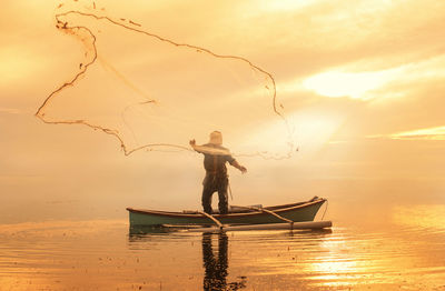 Fisherman with fishing net on boat in sea during sunset 