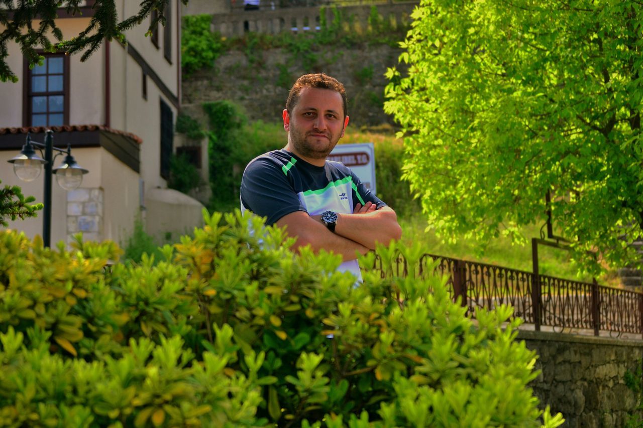 person, casual clothing, lifestyles, looking at camera, portrait, young adult, leisure activity, smiling, front view, full length, sitting, young men, green color, plant, happiness, standing, built structure