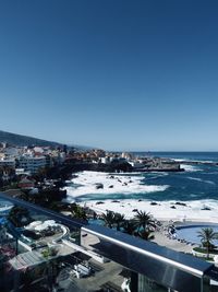 High angle view of city by sea against clear blue sky