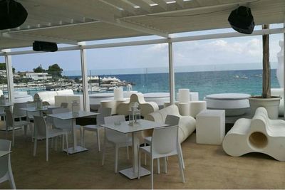 Chairs and table by sea against sky seen through window