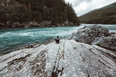 Rear view of person on rock by river against sky