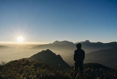 Rear view of man standing on mountain against clear sky