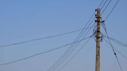 Low angle view of electricity pylon against clear blue sky