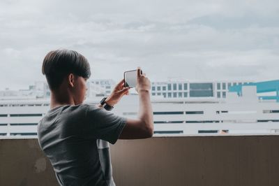 Man photographing with mobile phone against sky