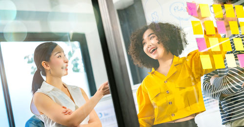 Smiling business colleagues discussing over adhesive notes in office