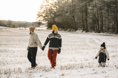 Gay couple holding hands while walking with daughter on snow during winter