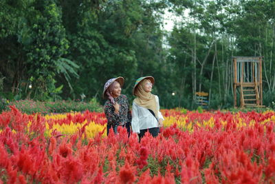 Rear view of women standing by flowering plants on field