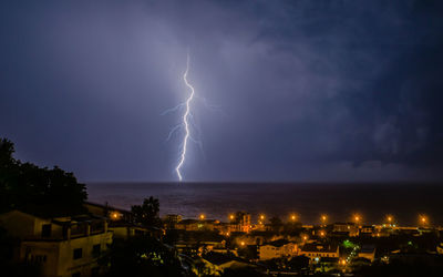 Lightning over illuminated cityscape against sky at night