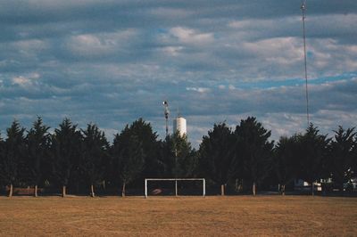 Trees on field against cloudy sky