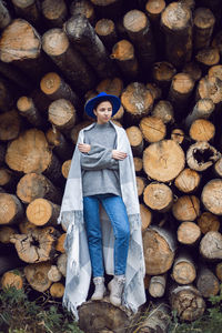 Woman director is standing by a log at a sawmill in a scarf and a blue hat in autumn