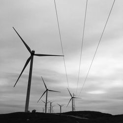 Low angle view of silhouette windmills against cloudy sky